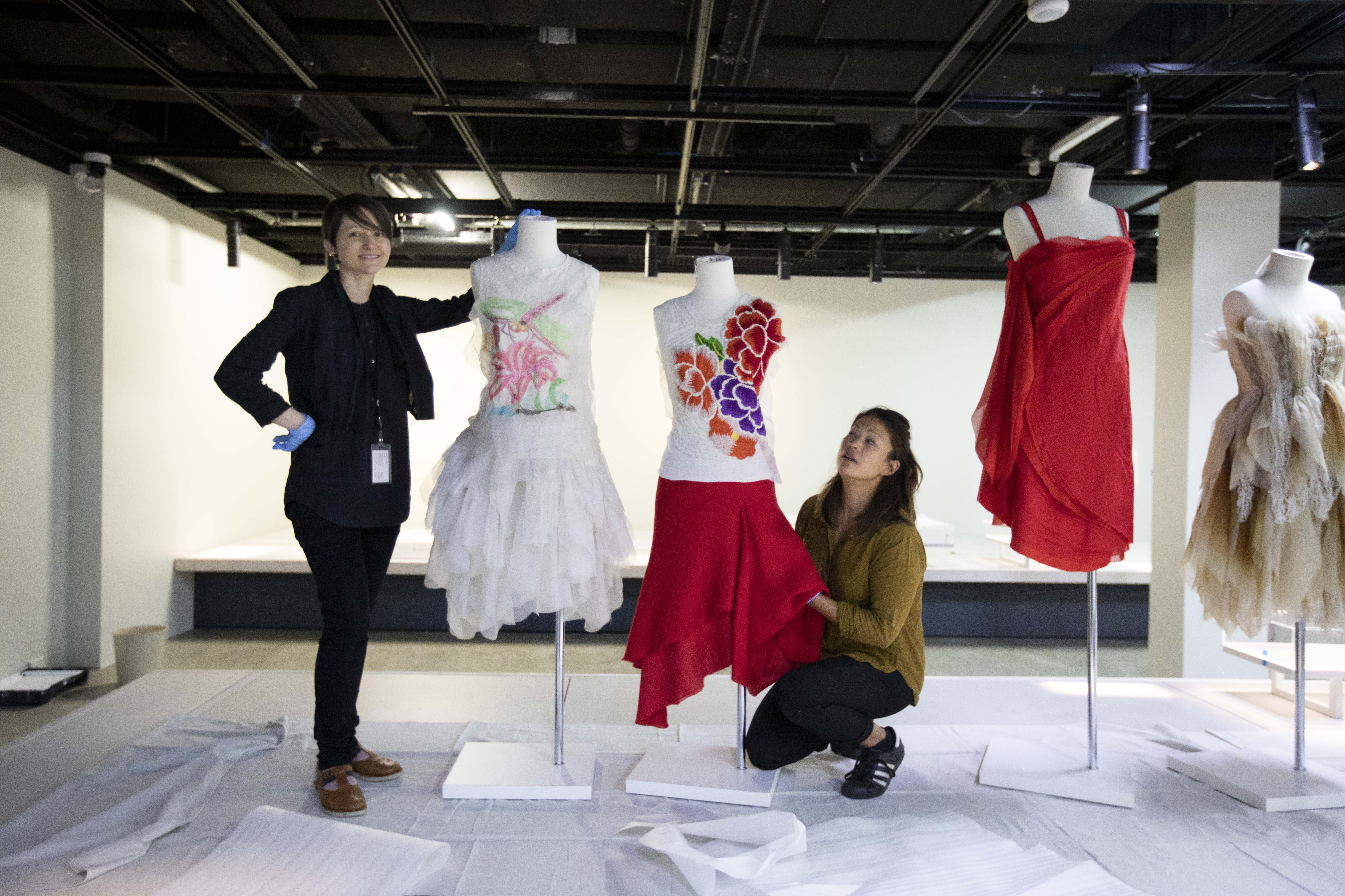 Two women in the process of placing the clothed dress forms into position on the display plinths.